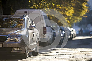 Long row of cars parked along roadside on sunny autumn day on blurred green golden foliage bokeh background. Transportation,