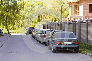 Long row of cars parked in quiet neighborhood on clean empty paved street along new stone fence on background of unfinished brick