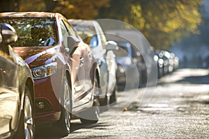 Long row of different shiny cars and vans parked along empty roa