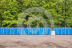 Long row of portable toilets in front of a forest where one has tipped over