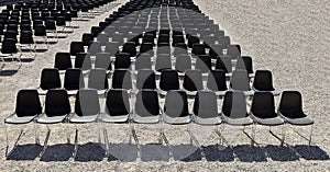 Long rows of empty black plastic chairs geometrically arranged under the sun. Copy space.