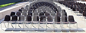 Long rows of empty black plastic chairs geometrically arranged under the sun.