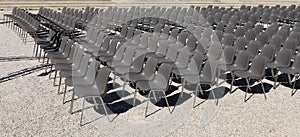 Long rows of empty gray plastic chairs geometrically arranged under the sun. Side view, copy space.