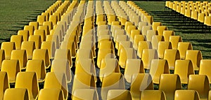 Long rows of empty yellow plastic chairs geometrically arranged on a lawn.