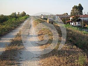 A long rural dirt road in perspective between a field and a row of houses