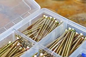 Long self-tapping screws in transparent plastic storage box on a wooden bench