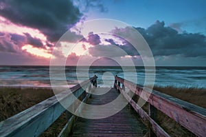 Long shot of a boardwalk leading to a beach with a colorful sunset in Wenningstedt, Sylt, Germany