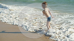 Long shot of happy kid splashing in sea on sandy beach