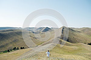 Long shot of a woman in a white dress standing on a hill ridge