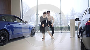 Long shot of young caucasian ballet dancers dancing in car dealership. Man and woman performing classic dance in auto