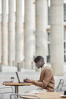 Long shot of young male solopreneur typing on laptop keyboard