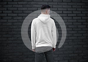 Long sleeve white mens clothing template on young guy on brick wall background, back view, blank hoodie with hood