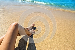 Long slim young woman legs relaxing lying down and sunbathing on sand tropical beach under hot sun in summer. Skincare, sun aging