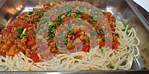 Long spaghetti sauteed tomato sauce with pork and chicken in white pan.