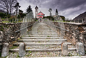 Long stairs leading up to an old rose colored church under an expressive overcast sky