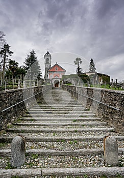 Long stairs leading up to an old rose colored church under an expressive overcast sky