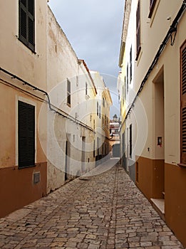 Long straight cobbled picturesque empty narrow street of old houses in cuitadella menorca