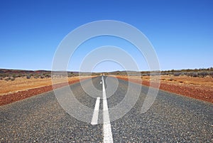 Long straight road in Australian Outback with read sand