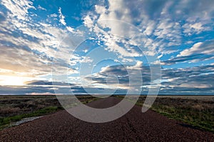 Long straight road disappears into the distant horizon under a sunset sky full of clouds in the outback