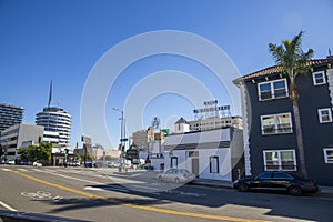 A long street lined with parked cars, office buildings, apartments, lush green palm trees and shops and cars driving