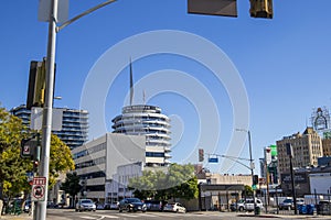 A long street lined with parked cars, office buildings, apartments, lush green palm trees and shops and cars driving