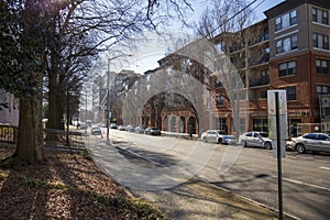 A long street with a red brick apartment buildings, shops, parked cars and bare winter trees in Atlanta Georgia