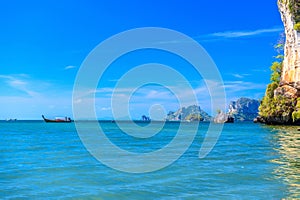 Long tail boat in bay of sea with rocks cliffs in background, To