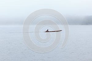 Long tail boat with a fisherman inside on river with foggy background.