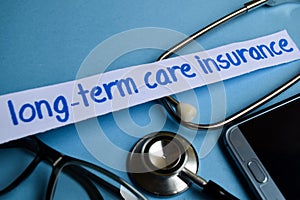 Long-term care insurance inscription with the view of stethoscope, eyeglasses and smartphone on the blue background