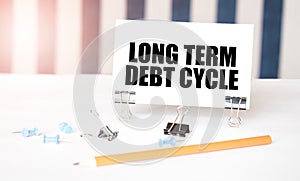 LONG TERM DEBT CYCLE sign on paper on white desk with office tools. Blue and white background