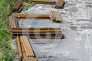 Long and thick, rust-covered steel bars stacked outside on a gravel square, viewed from above.