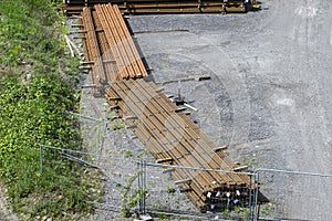 Long and thick, rust-covered steel bars stacked outside on a gravel square, viewed from above.