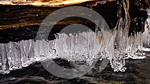 Long thin icicles hang above rapids on of mountain stream. Winter season at river