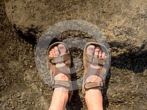 Long tired naked legs in hiking sandals on peak. Hiking in sandstone rocks, hilly landscape