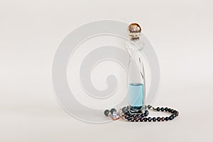 A long transparent glass of perfume that is half filled with blue - teal liquid is standing. A round golden lid is on top of it.