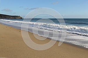 Long, unbroken line of white surf on a deserted beach