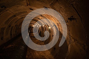 Long underground round concrete tunnel with a pipe, lit by incandescent lamps. Underground tunnel of a heating main or a water