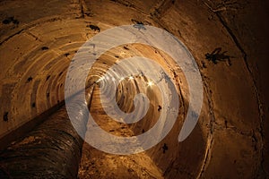 Long underground round concrete tunnel with a pipe, lit by incandescent lamps. Underground tunnel of a heating main or a water