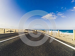Long way road for travel car transportation concept with desert and beach on the side - sea water and blue clear beautiful sky in