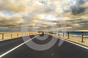 Long way road for travel car transportation concept with desert and beach on the side - sea water and cloudy beautiful sky in