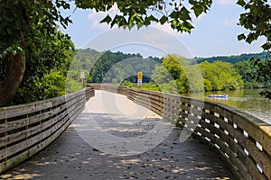 A long winding boardwalk along the river with a wooden rail along the sides with vast still river water, lush green trees