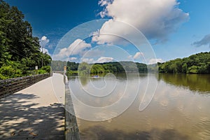 A long winding boardwalk along the river with a wooden rail along the sides with vast still river water, lush green trees