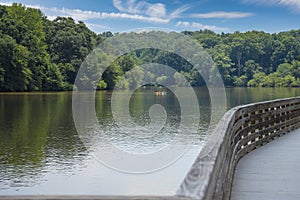 A long winding boardwalk along the river with a wooden rail along the sides with vast still river water, lush green trees