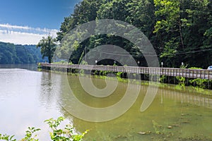 A long winding boardwalk along the river with a wooden rail along the sides with vast still river water, lush green trees