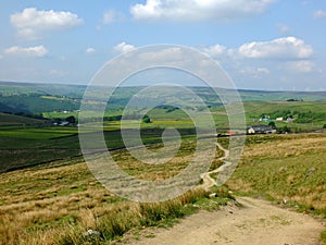 A long winding footpath running downhill in stoodley moor in yorkshire with fields and farms in the distance with pennine hills