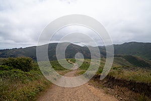 Long, winding hiking trail leading to mountains with two hikers marching into distance