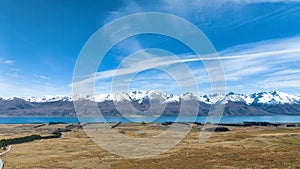 Long winding narrow gravel road across remote agricultural countryside towards the snow capped Southern alps mountain range