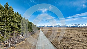 Long winding narrow gravel road throiugh rural agricultural countryside towards the snow capped Southern alps mountain range