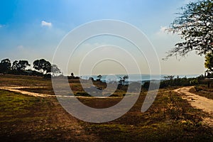 Long and winding rural road crosses the hills in the summer farm field with blue sky background and copy space for text.