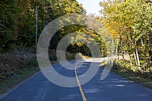 Long winding rural road surrounded by trees on a beautiful warm sunny fall day in Muskoka, Ontario